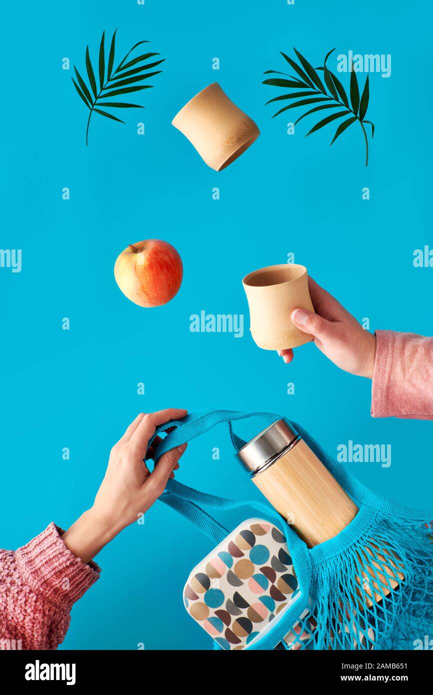 Kein Abfall von Tee in einem umweltfreundlichen, isolierten Bambuskolben. Zwei Hände mit Tasse und Palmblatt, Netztasche mit Lunchbox und Teeklasche fliegen. Kein Wast Stockfoto