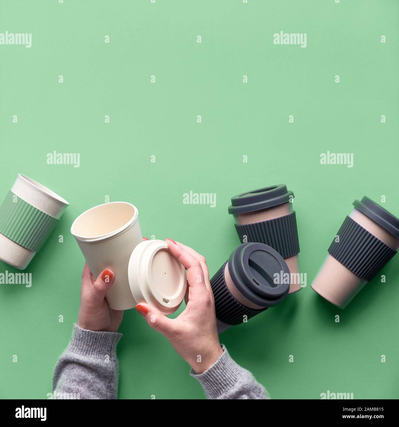 Verschiedene Bambusreisen wiederverwendbare Kaffee- oder Teetassen oder Magen mit Silikonisolierung auf grünem Minzgrund. Hände öffnen den Deckel auf einem Becher. Umweltfreundlich Stockfoto
