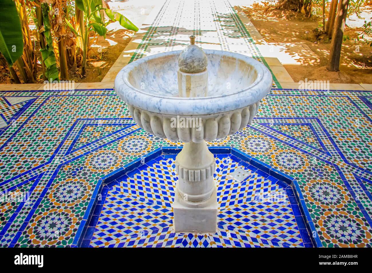Weißer Steinbrunnen inmitten des grünen Gartens des islamischen Palastes. Es ist in Marokko. Der Brunnen steht auf blau-weißen Fliesen mit typisch arabischem und Stockfoto