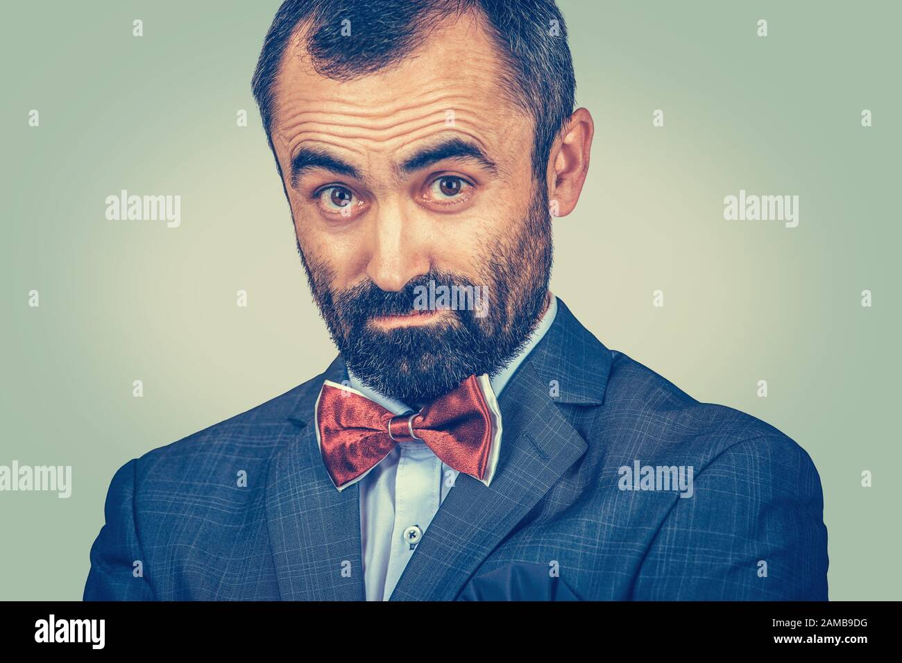 Nahaufnahmen von zweifelhaftem, verdächtigem Mann im dunklen Anzug, weißem Hemd, roter Schleife. Bärtiger Geschäftsmann, der staunend aussieht und um Kamera bittet. Eine Pers Stockfoto