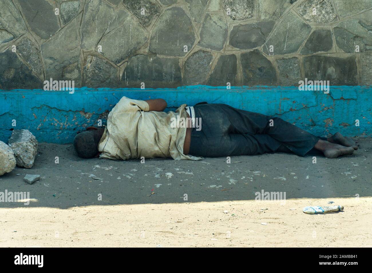 Ein obdachloser kenianischer Mann, der im Schatten eines Gebäudes auf einem sandigen und staubigen Straßenbelag schläft, Mombasa, Kenia Stockfoto