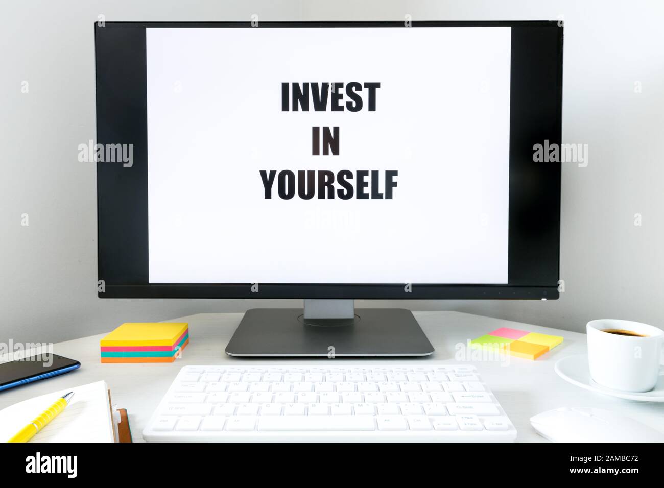 Auf dem Monitor angezeigten Text In Sich Selbst Investieren. Schreibtisch mit Tastatur, Bürozubehör und einer Tasse Kaffee. Das Konzept des persönlichen und des Profess Stockfoto