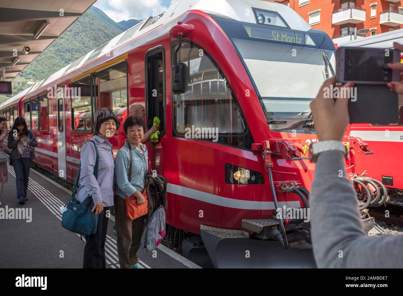 Chinesische Touristen machen neben einem Schweizer Zug, der nach St. Moritz fährt, ein Bild. Bahnhof von Tirano, Italien Stockfoto