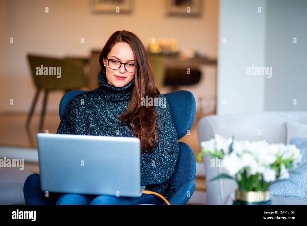 Schuss einer lächelnden jungen Frau mit ihrem Laptop, während sie auf dem Stuhl sitzt und von zu Hause aus arbeitet. Stockfoto
