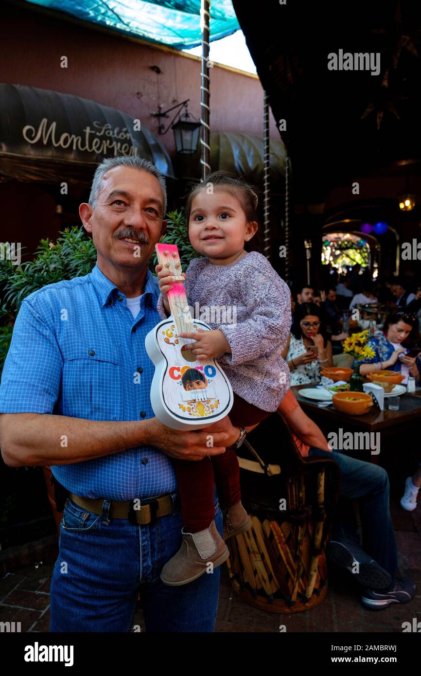 Großvater hält seine Enkelin in einem Restaurant in Tlakquepaque, Mexiko. Sie spielt ihre Spielzeuggitarre Stockfoto