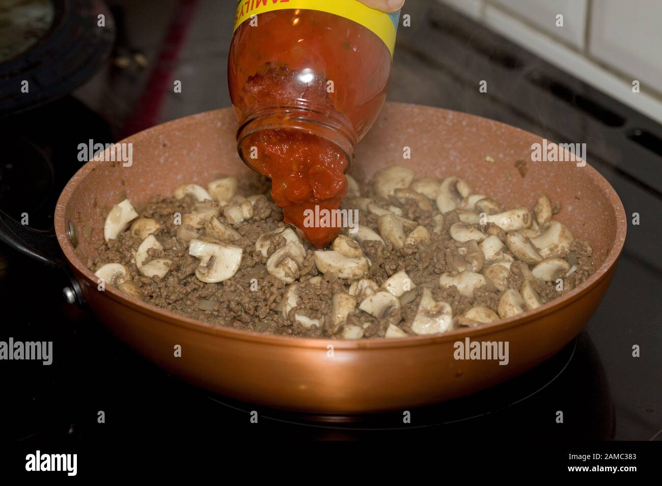 Hinzufügen von Bolognese-Sauce zu gemahlenem Hackfleisch und Champignons, die in der Pfanne zubereitet werden Stockfoto
