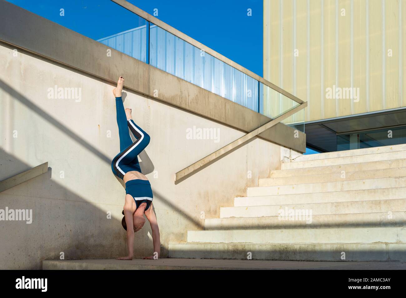 Frau, die einen Handstand auf einer Treppe draußen macht, moderne Architektur. Stockfoto