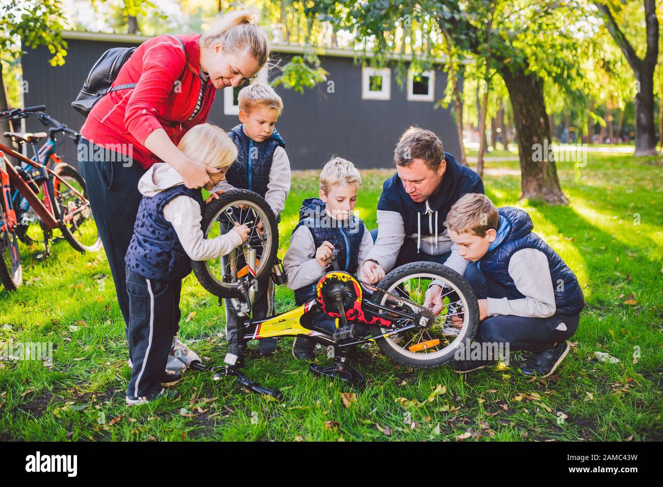 Das Thema ist Teamarbeit und ein enger Familiengeist. Probleme gemeinsam lösen. Große, freundliche Familie, die ein Fahrrad im Park repariert. Vater und Mutter unterrichten Stockfoto