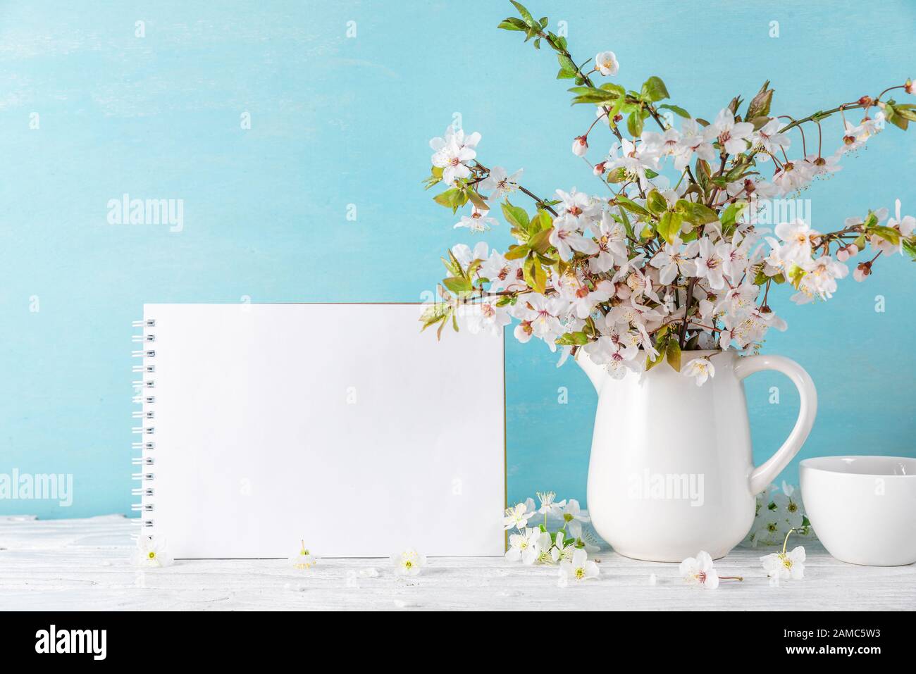 Stillleben mit schöner Frühlingskirschblüte, Kaffeetasse und leerer Grußkarte auf blauem Hintergrund. Verspotten. Ferien- oder Hochzeitskonzept Stockfoto