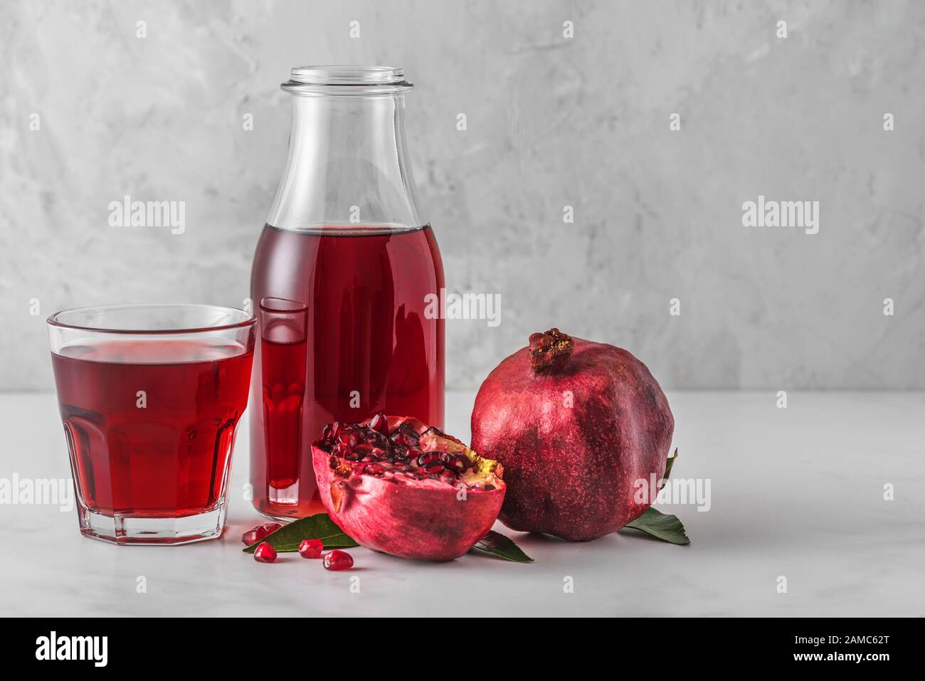 Granatapfelsaft in einer Flasche mit einem Glas Saft und frischen Granatapfeln auf dem Marmortisch. Konzept für gesunde Getränke Stockfoto