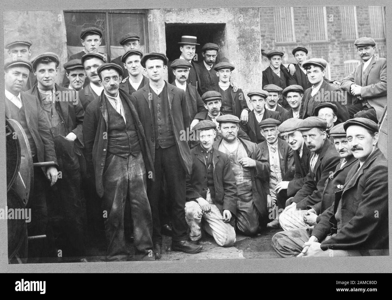 Arbeitnehmer, soziale Struktur. Oberbeleuchter, Boss, Tuch, Kappe, Chef. Viktorianische Gruppe von Arbeitern in der traditionellen Arbeitskleidung außerhalb einer Fabrik. Stockfoto