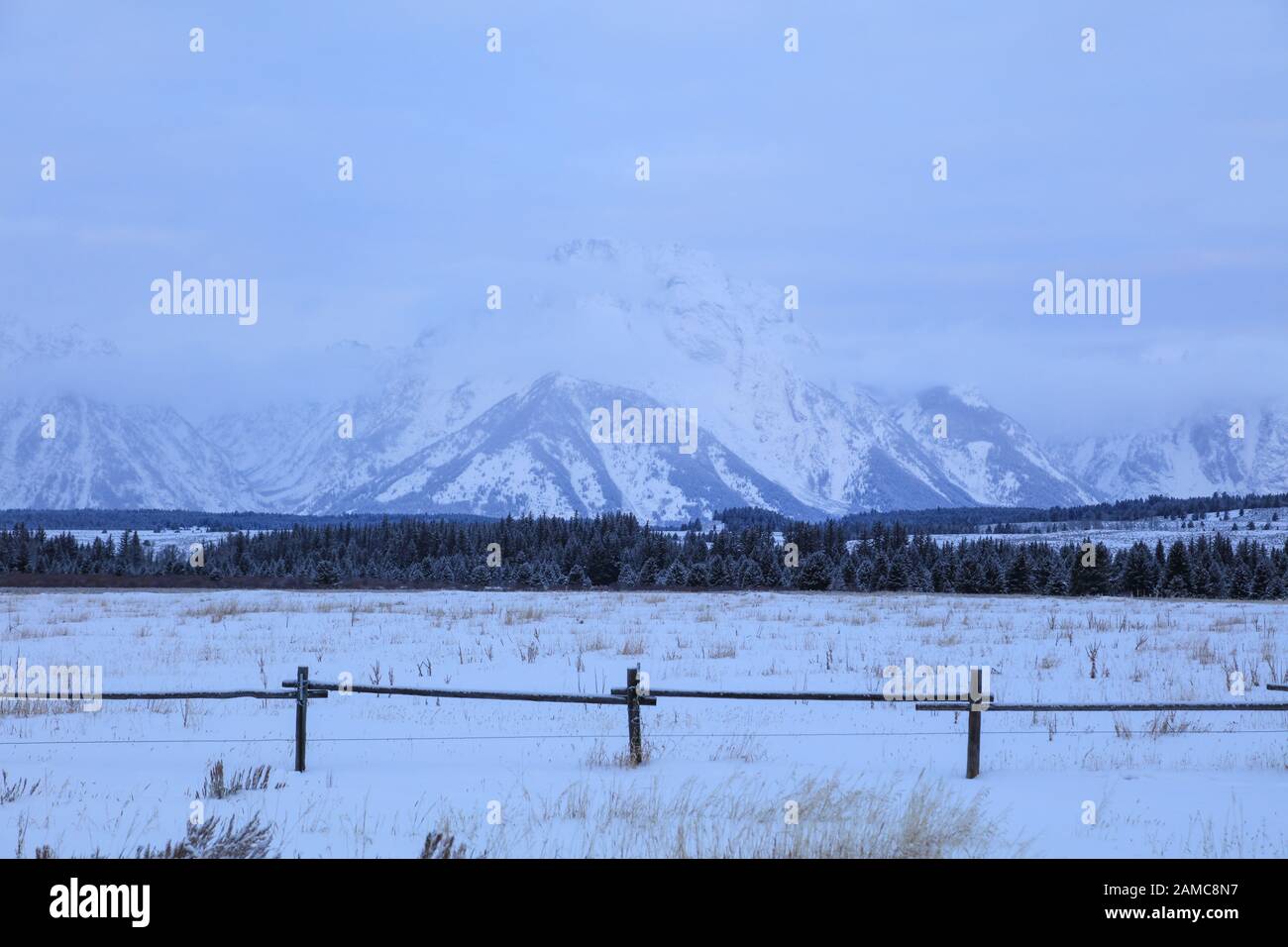 Schnee und Nebel bedeckten den Mount Moran im Winter mit einem straßenseitigen Holzzaun im Grand Teton National Park, Wyoming Stockfoto