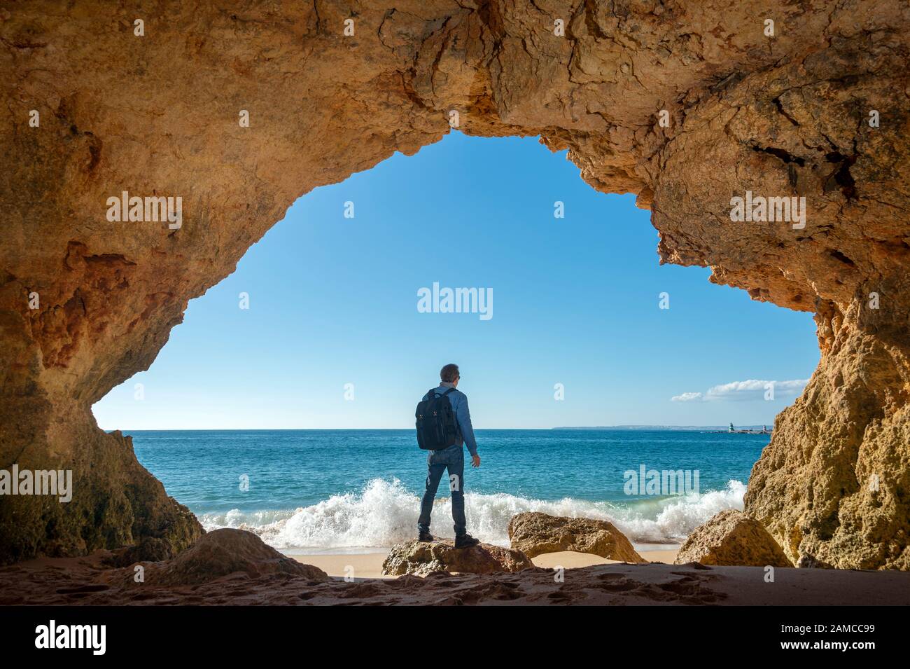 Mann mit Rucksack in einer Höhle mit Blick auf das Meer, Abenteuer Trekking. Stockfoto