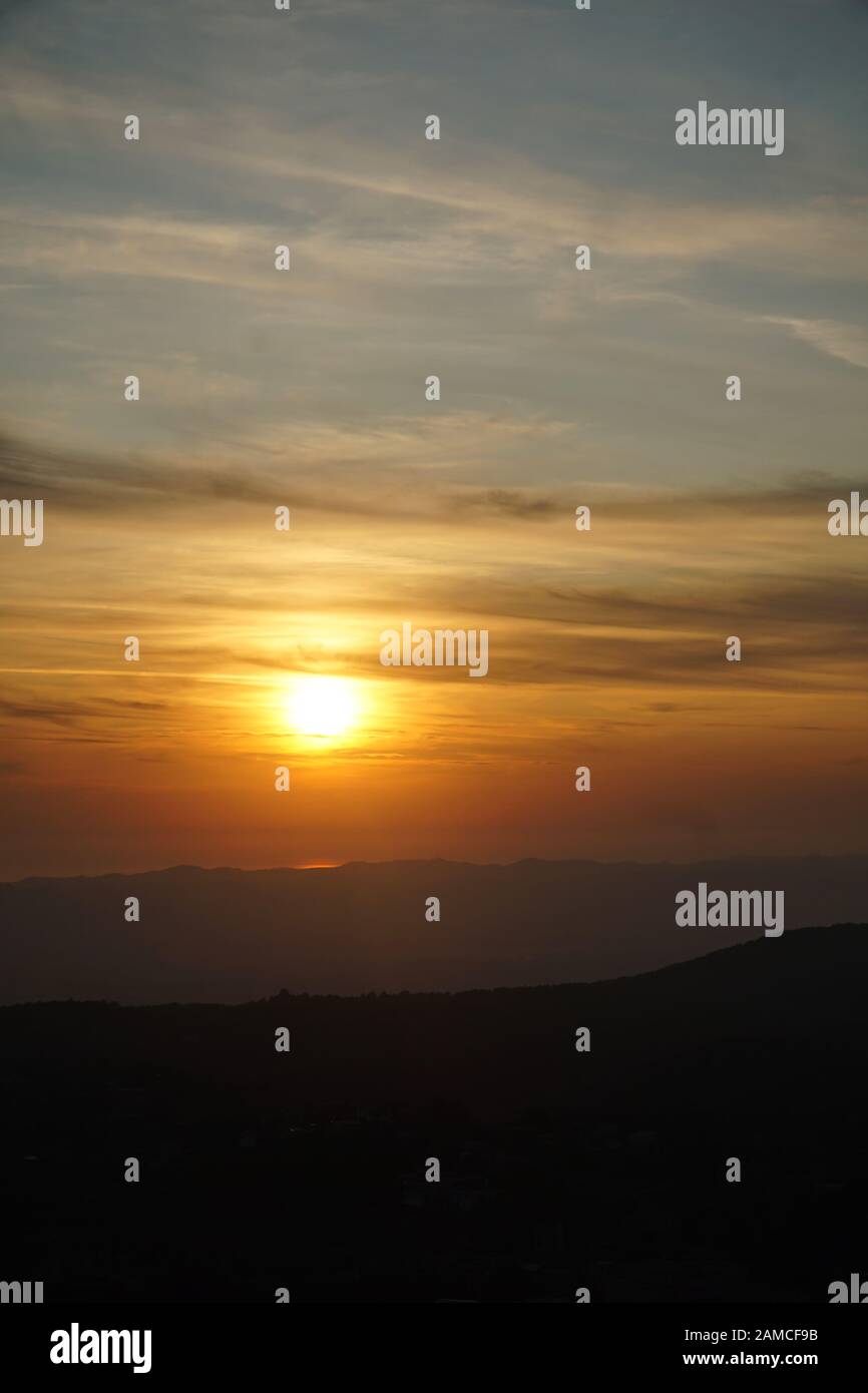 Atemberaubender Sonnenuntergang über dem Meer mit hellem Spiegelbild und einer Gebirgskette vor, dunkle Wolken am Himmel. Vertikales Bild. Stockfoto