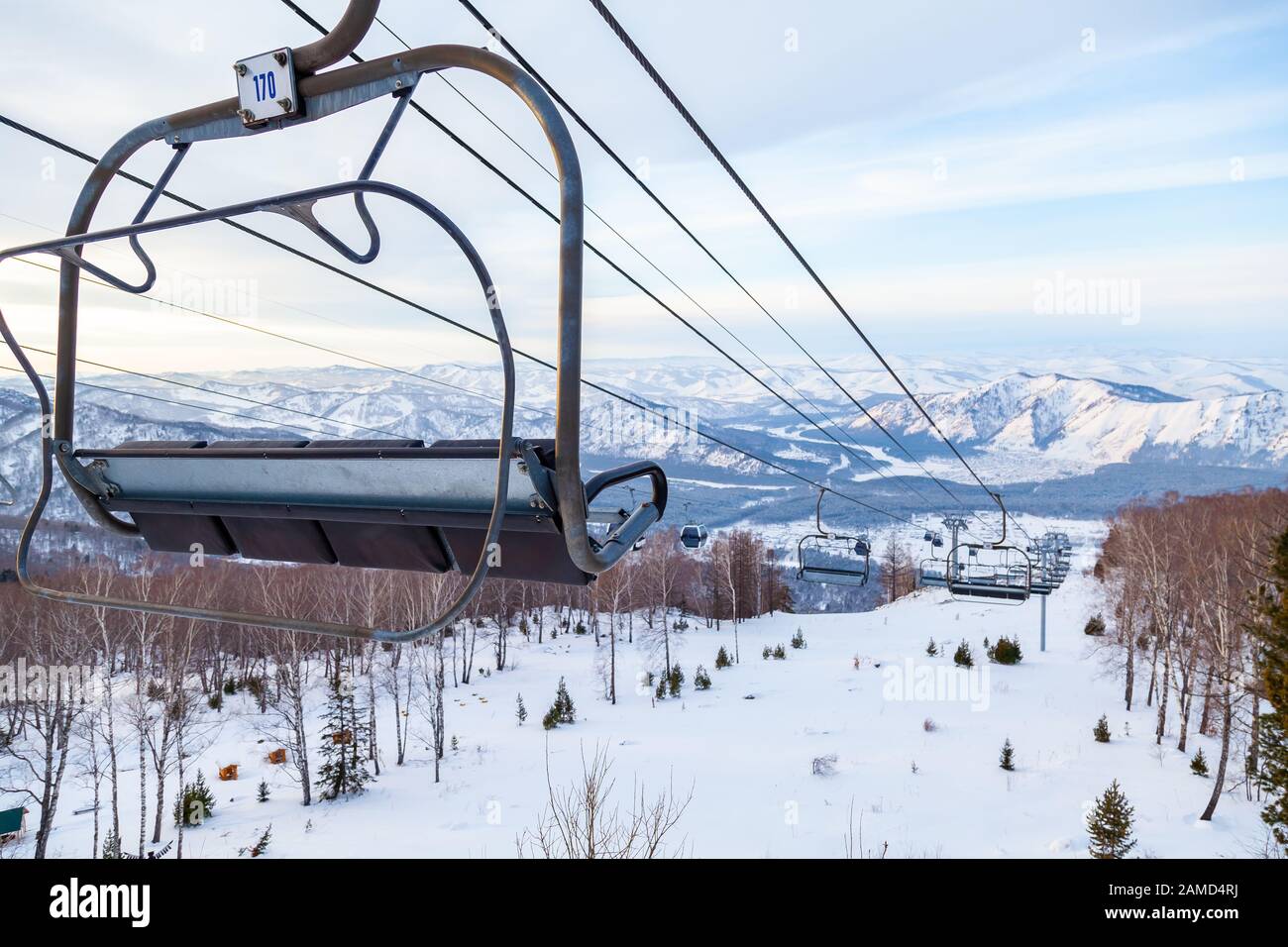 Eine Skilift-Sessellbahn mit einer Kabine, die an einem Kabel aufgehängt ist, in der Menschen mit Skiern und Snowboards auf einem Hintergrund von Bergen sitzen, Bäume mit Sno Stockfoto