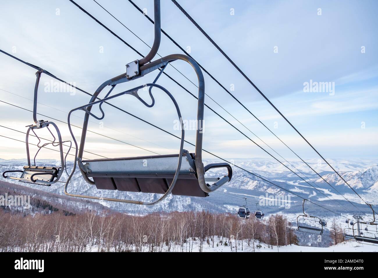 Eine Skilift-Sessellbahn mit einer Kabine, die an einem Kabel aufgehängt ist, in der Menschen mit Skiern und Snowboards auf einem Hintergrund von Bergen sitzen, Bäume mit Sno Stockfoto