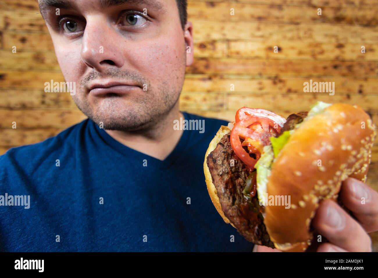 Fröhlicher Mann mit seinem Fast-Food-Burger. Nicht so viel gesunder Lebensstil, aber was auch immer! Stockfoto