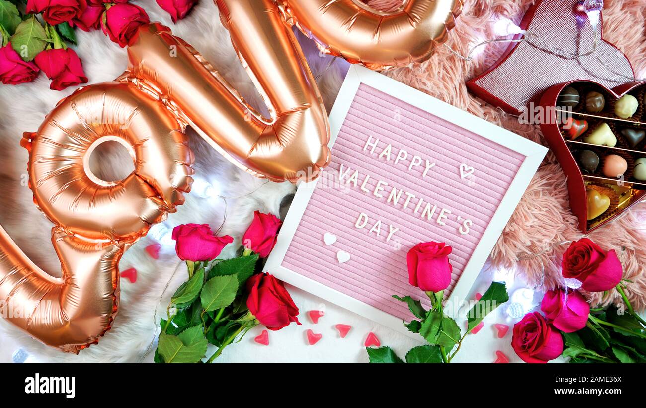 Fröhliche Valentinstag flach lag oben mit Rosen, Schoko-Geschenkbox und Briefpapier mit Grußtext und großen Rosengoldballons in Form von TH Stockfoto