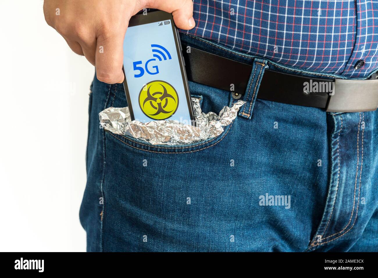 5g Netzgefährdungskonzept. Mann steckt ein Smartphone in seine Tasche, die mit Aluminiumfolie bedeckt ist, um das Signal zu blockieren. Das Gefahrenschild wird auf dem Telefon angezeigt. Stockfoto