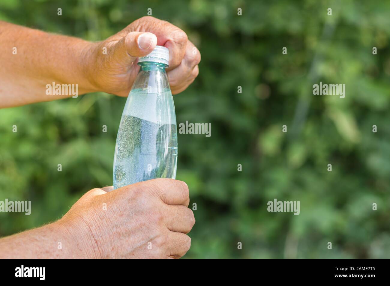 Man's Hands öffnet eine Flasche Mineralwasser vor grünem natürlichen Hintergrund Stockfoto