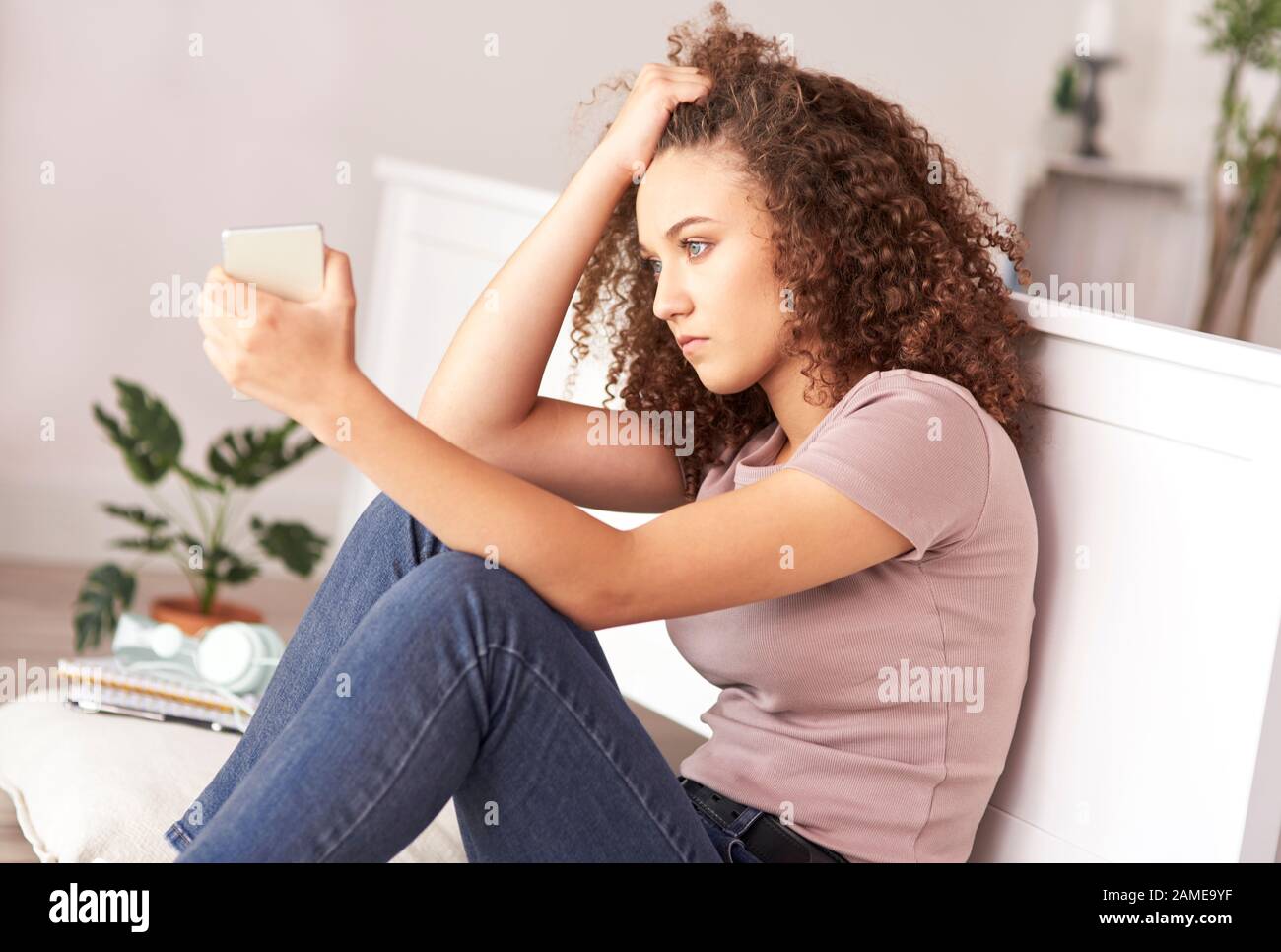 Trauriges Mädchen im Teenager-Alter, das auf dem Bett in ihrem Zimmer sitzt Stockfoto