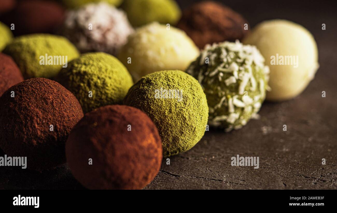 Bunte, hausgemachte Trüffeln mit Kakaopulver, Matcha-Teepulver, zerfetzter Kokokuss auf dunklem Hintergrund. Kopierbereich für Text oder Design, Banner. Stockfoto