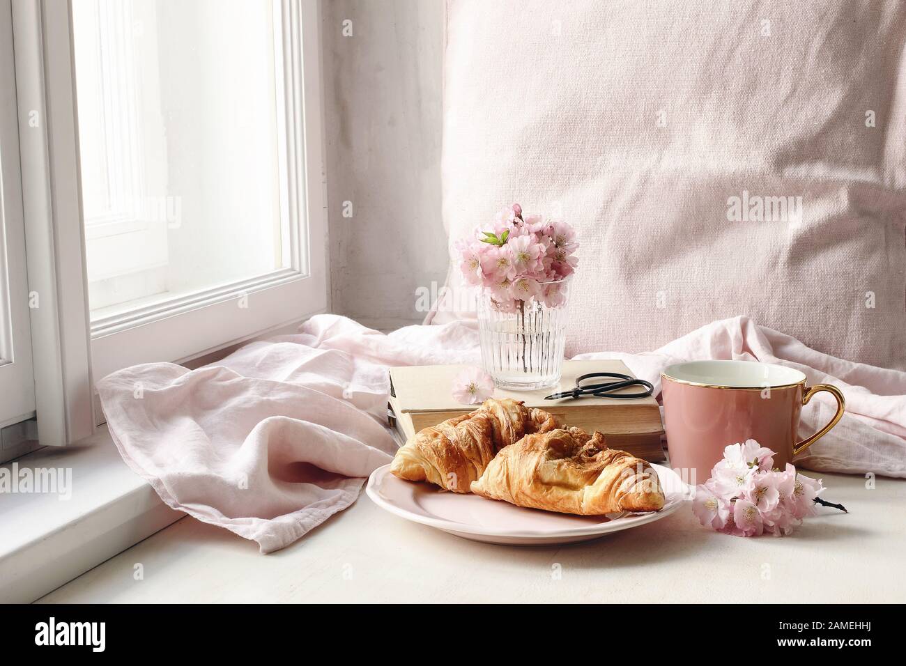 Frühlingsszene im Stillleben. Tasse Kaffee, Croissant Gebäck, alte Bücher und Scheren, feminines Foto im Vintage-Stil. Blumenapposition mit rosafarbenem Sakura, Stockfoto