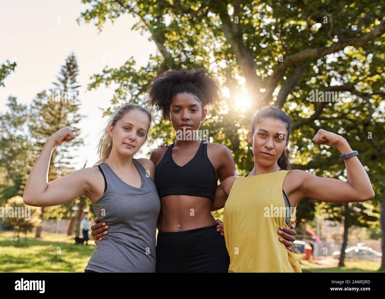 Sportlich gesunde junge multiethnische Frauenfreunde, die ihre Muskel mit Blick auf die Kamera im Park biegen - starke Frau, die weibliche Macht zeigt Stockfoto
