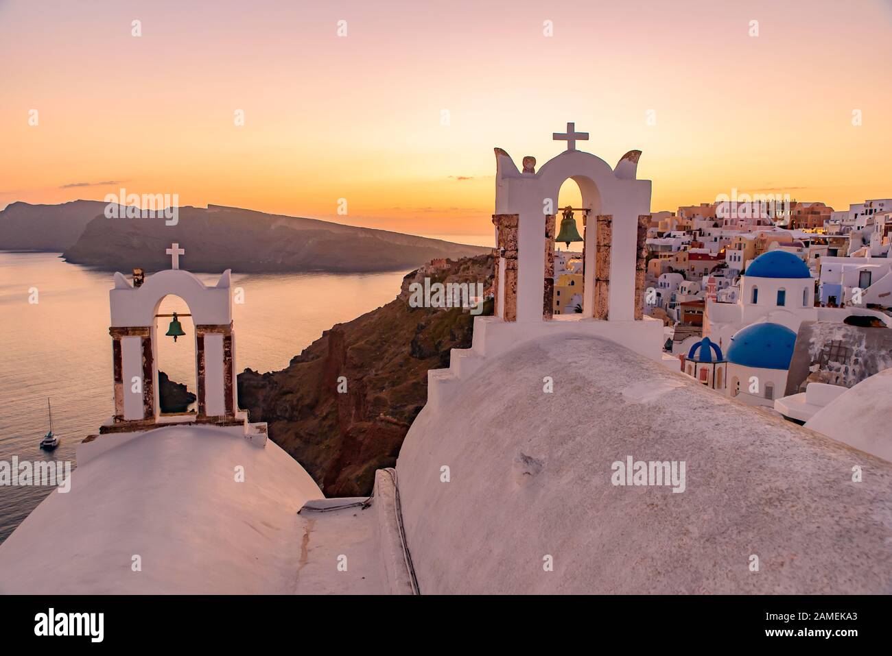 Blaue Kuppelkirchen und der Kirchturm mit Blick auf die ägeische See mit warmem Licht bei Sonnenuntergang in Oia, Santorini, Griechenland Stockfoto