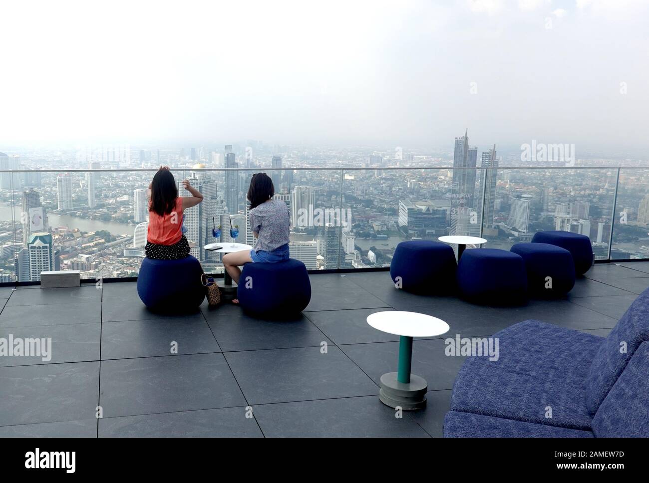 Zwei Frauen sitzen auf dem Dach der King Power MahaNakhon Gebäude mit blauen Getränke auf den Tisch und beobachtete Bangkok Stadtbild. Stockfoto