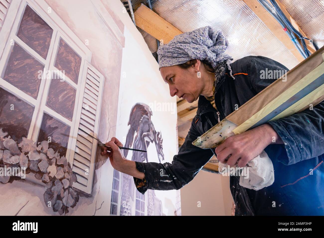 Frauenkünstlerin malt eine Wand in einem Wohnzimmer. Das Wandbild widmet sich den Eindrücken von Paris. Der Autor zeichnet ein Detail - Fensterläden. Untere Ansicht. Stockfoto