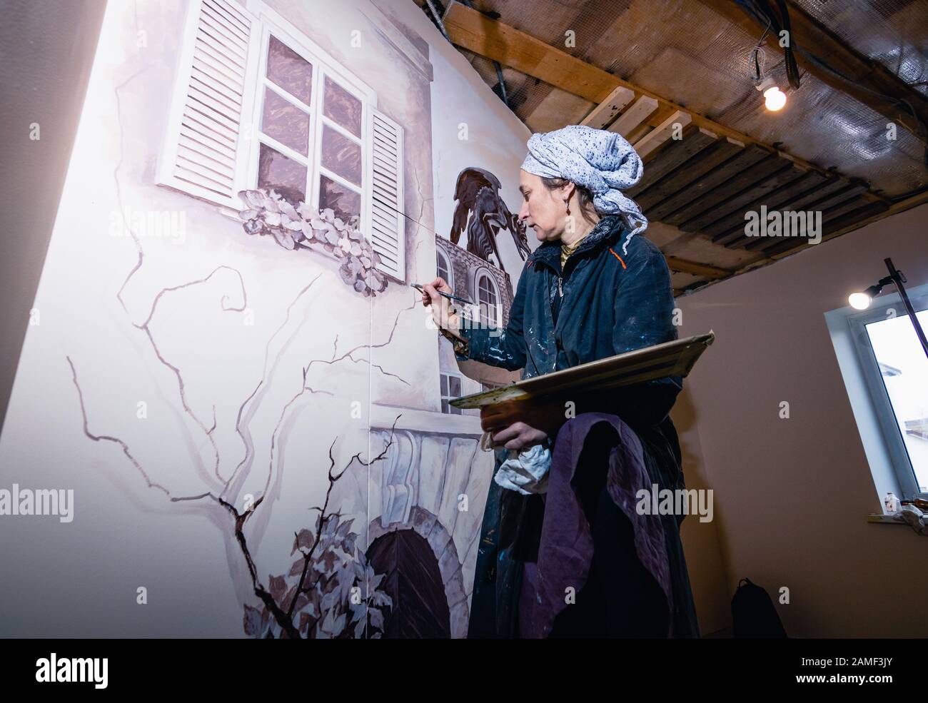 Frauenkünstlerin malt eine Wand in einem Wohnzimmer. Das Wandbild widmet sich den Eindrücken von Paris. Der Autor zeichnet ein Detail - Fensterläden Stockfoto