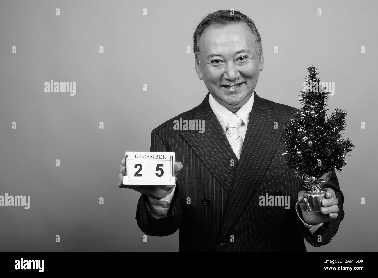 Studio mit einem Foto eines reifen asiatischen Geschäftsmannes, der vor grauem Hintergrund in Schwarzweiß zu Weihnachten bereit ist Stockfoto