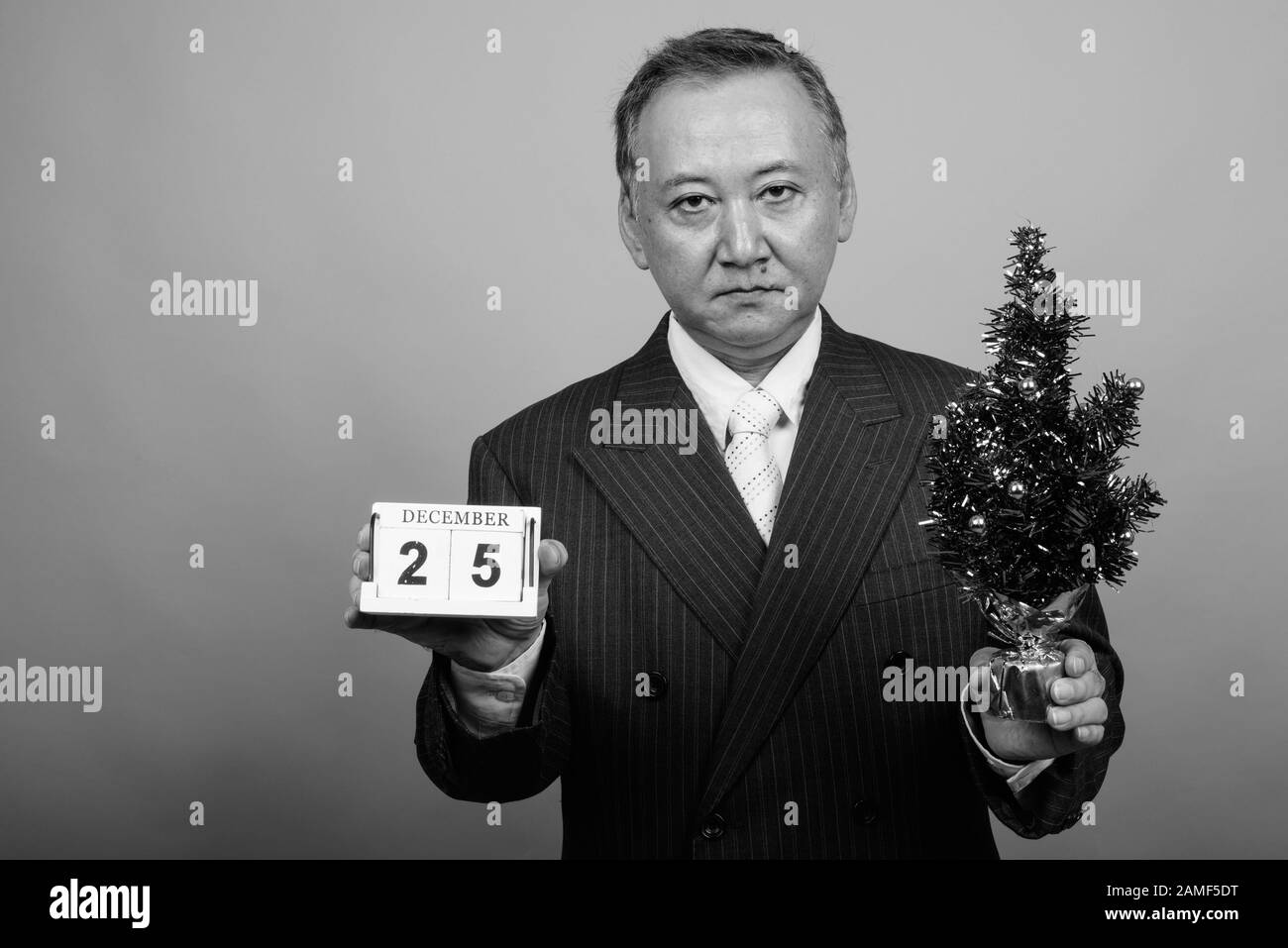 Studio mit einem Foto eines reifen asiatischen Geschäftsmannes, der vor grauem Hintergrund in Schwarzweiß zu Weihnachten bereit ist Stockfoto