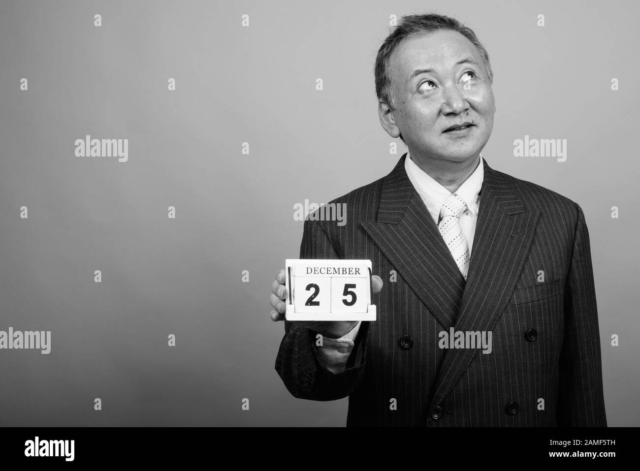 Studio mit einem Foto eines reifen asiatischen Geschäftsmannes, der vor grauem Hintergrund in Schwarzweiß zu Weihnachten bereit ist Stockfoto