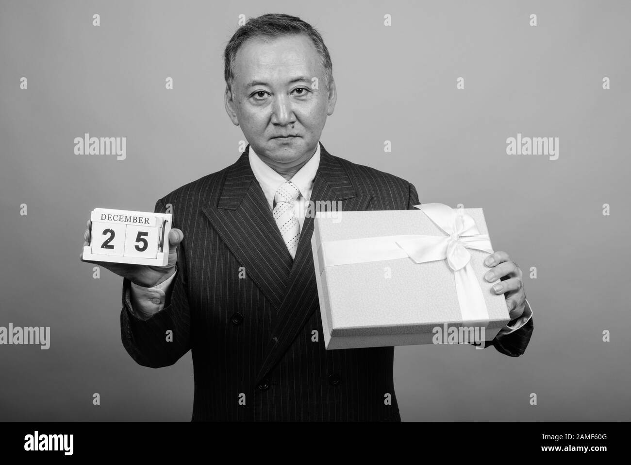 Studio mit einem Foto eines reifen asiatischen Geschäftsmannes, der vor grauem Hintergrund in Schwarzweiß zu Weihnachten bereit ist Stockfoto