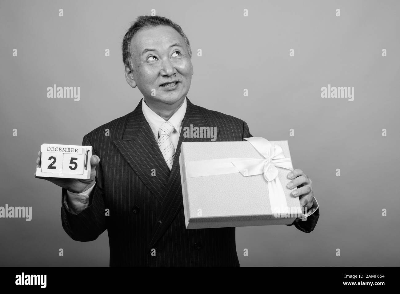 Studio mit einem Foto eines reifen asiatischen Geschäftsmannes, der vor grauem Hintergrund in Schwarzweiß zu Weihnachten bereit ist Stockfoto