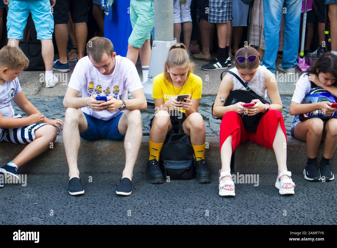 St. Petersburg, Russland, 28. Juli 2019. Gruppe Teenager sitzen mit Handys auf dem Bürgersteig während Marine Tag Stockfoto