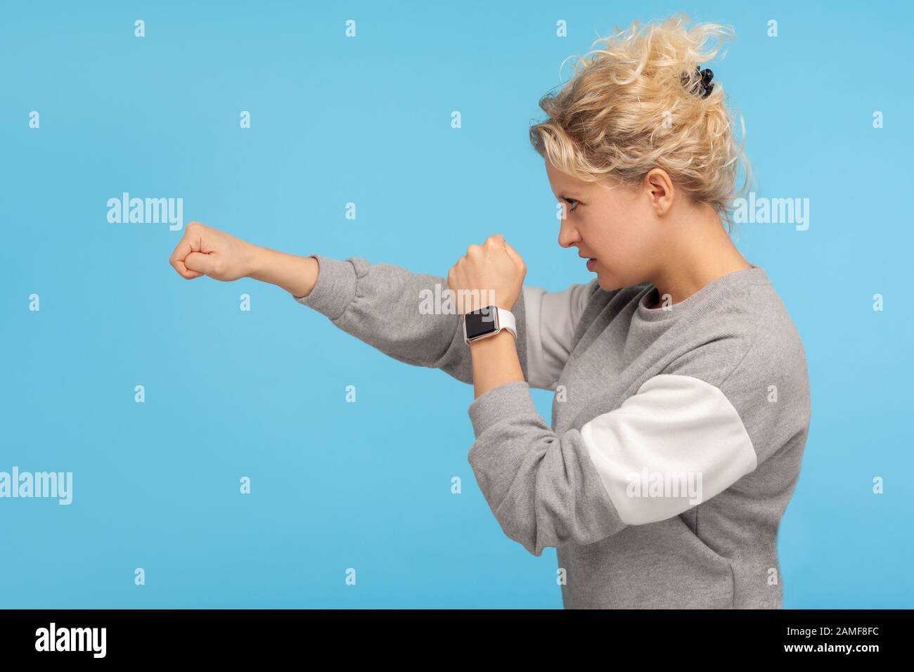 Bereit zum Kampf! Seitenansicht einer feistigen Frau mit kurzen lockigen Haaren im Sweatshirt, das mit aggressivem wütenden Ausdruck zur Seite schlägt, mit der Faust ausknockern. I Stockfoto