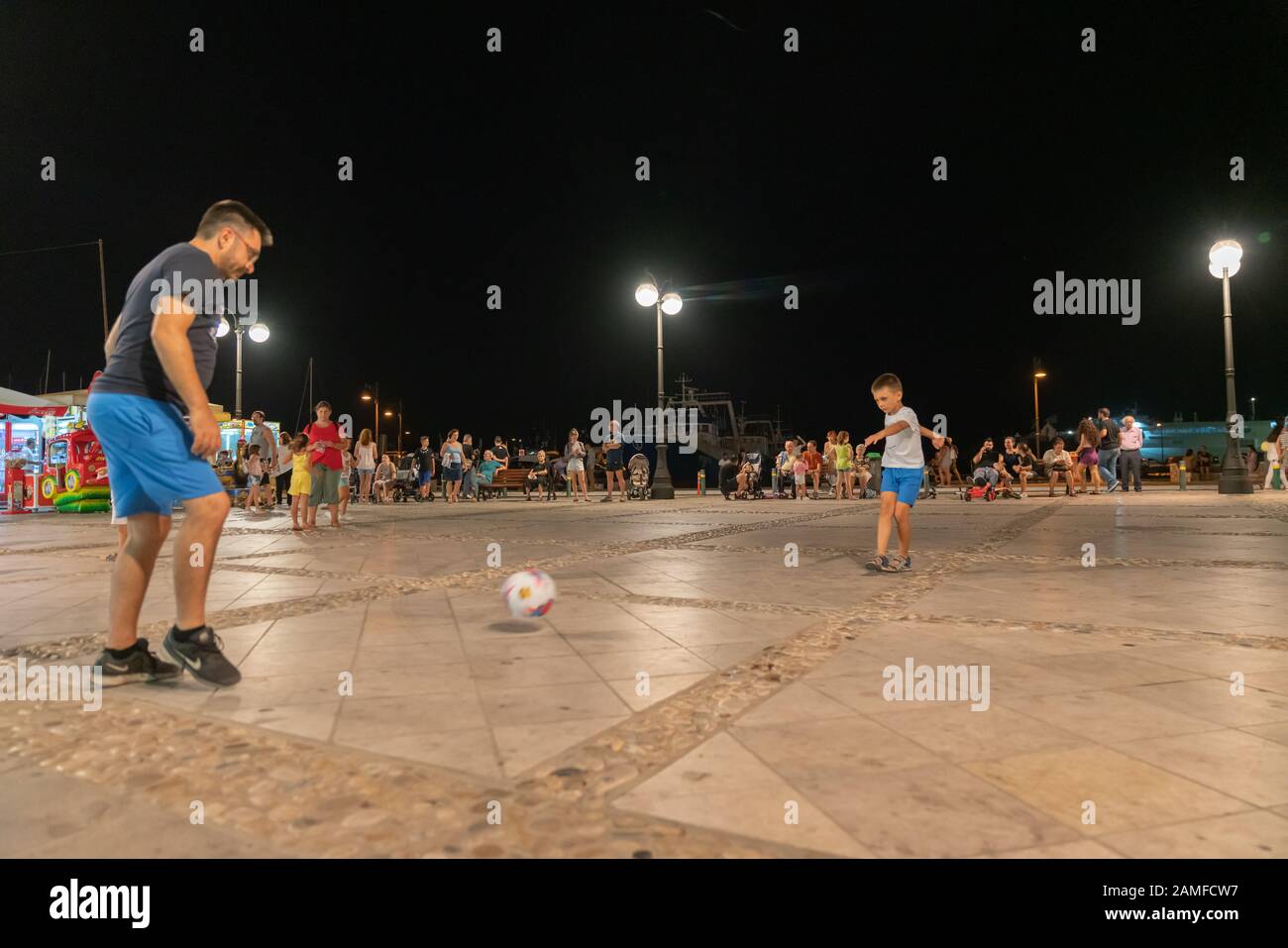 Naxos Griechenland - 11. August 2019; Junge und Vater spielen nachts auf dem Platz Fußball mit Schwerpunkt Junge. Stockfoto