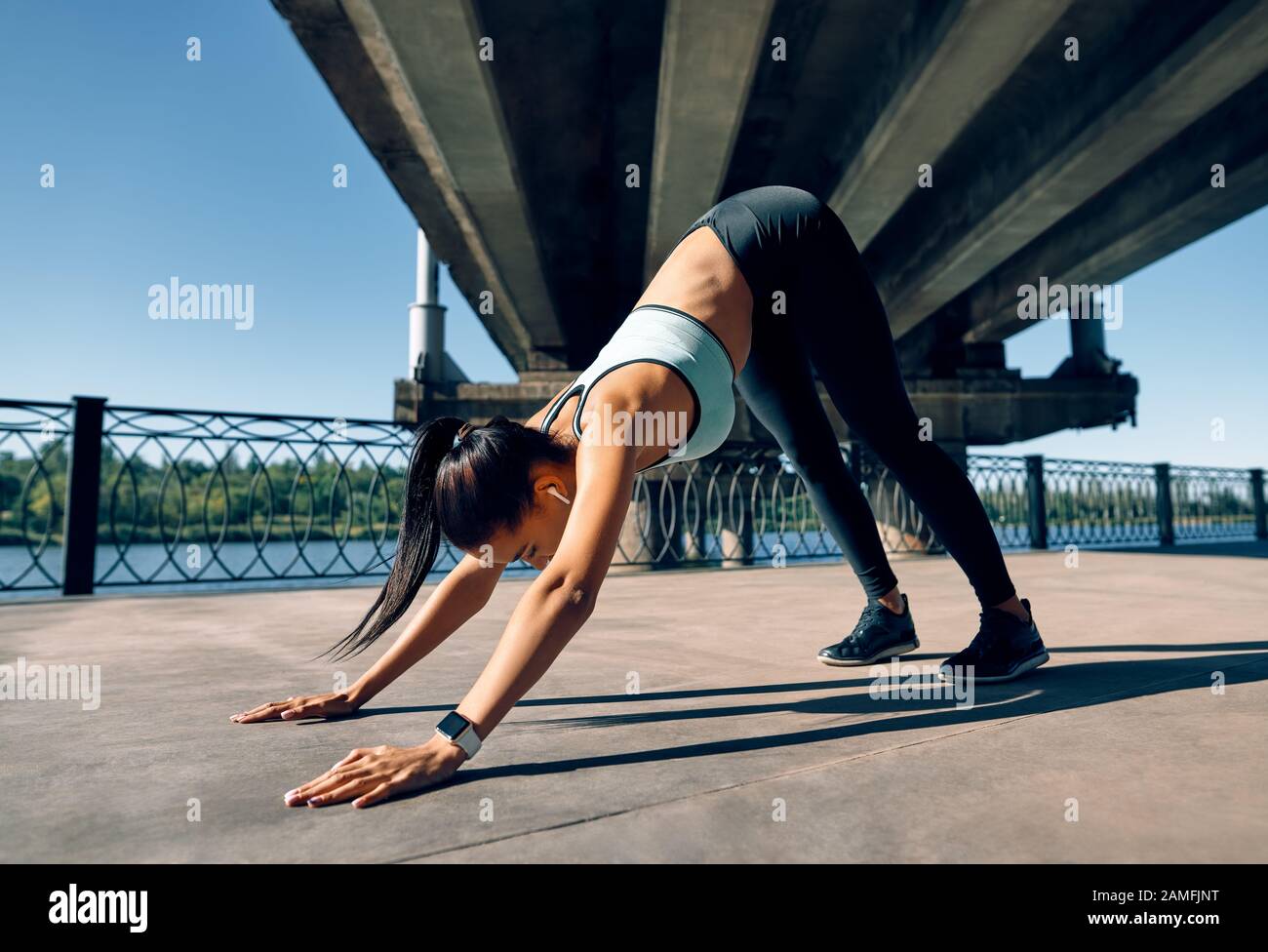 Junge sportliche Frau macht Yoga asana nach unten gerichteten Hund unter Industriebrücke. Adho Mukha Shvanasana Stockfoto