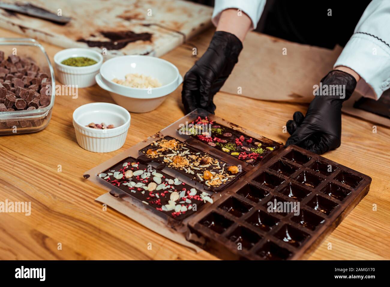 3/4-Blick auf Chocolatier in schwarzen Latexhandschuhen, die Schokoladenformen mit zubereiteten Schokoladenriegeln halten Stockfoto