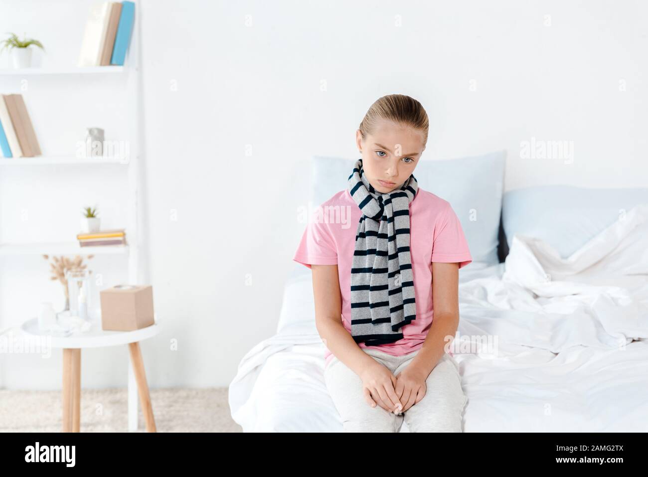 Krankes Kind im Schal, das zu Hause auf dem Bett sitzt Stockfoto