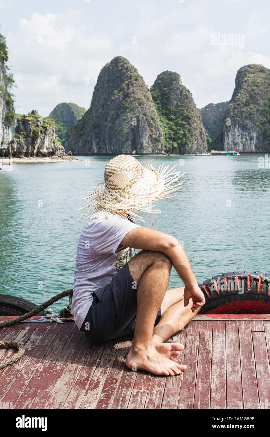 Junger Mann in einem Strohhut, der die Bootstour in Lan ha Bay, Cat Ba Island, Vietnam, genießt. Vertikale Ausrichtung Stockfoto