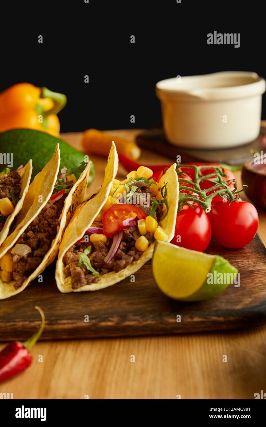 Leckere Tacos mit Limetten- und Kirschtomaten auf Holztisch auf schwarzem Grund Stockfoto