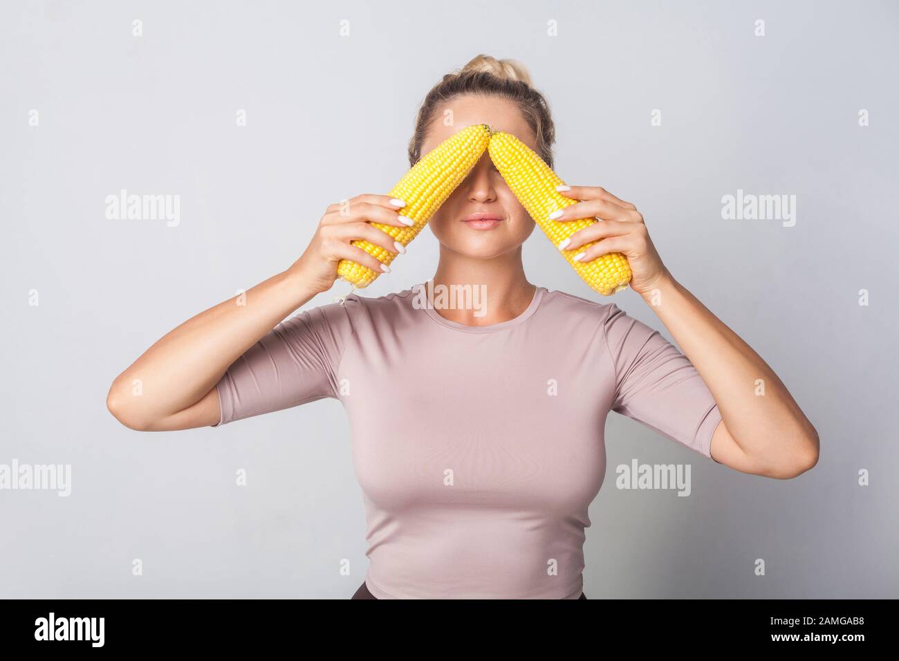 Portrait einer positiven Frau, die Augen mit Maiskolben, frischem Rohgemüse, gesundem Essen und vegetarischer Kost bedeckt, kalorienarme Lebensmittel nutriti Stockfoto