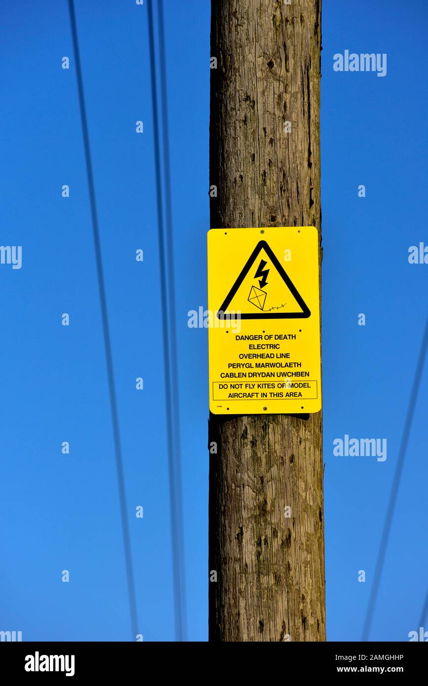 Warnschild für die Elektrizität über dem Kopf an einem Holzmast, Großbritannien Stockfoto