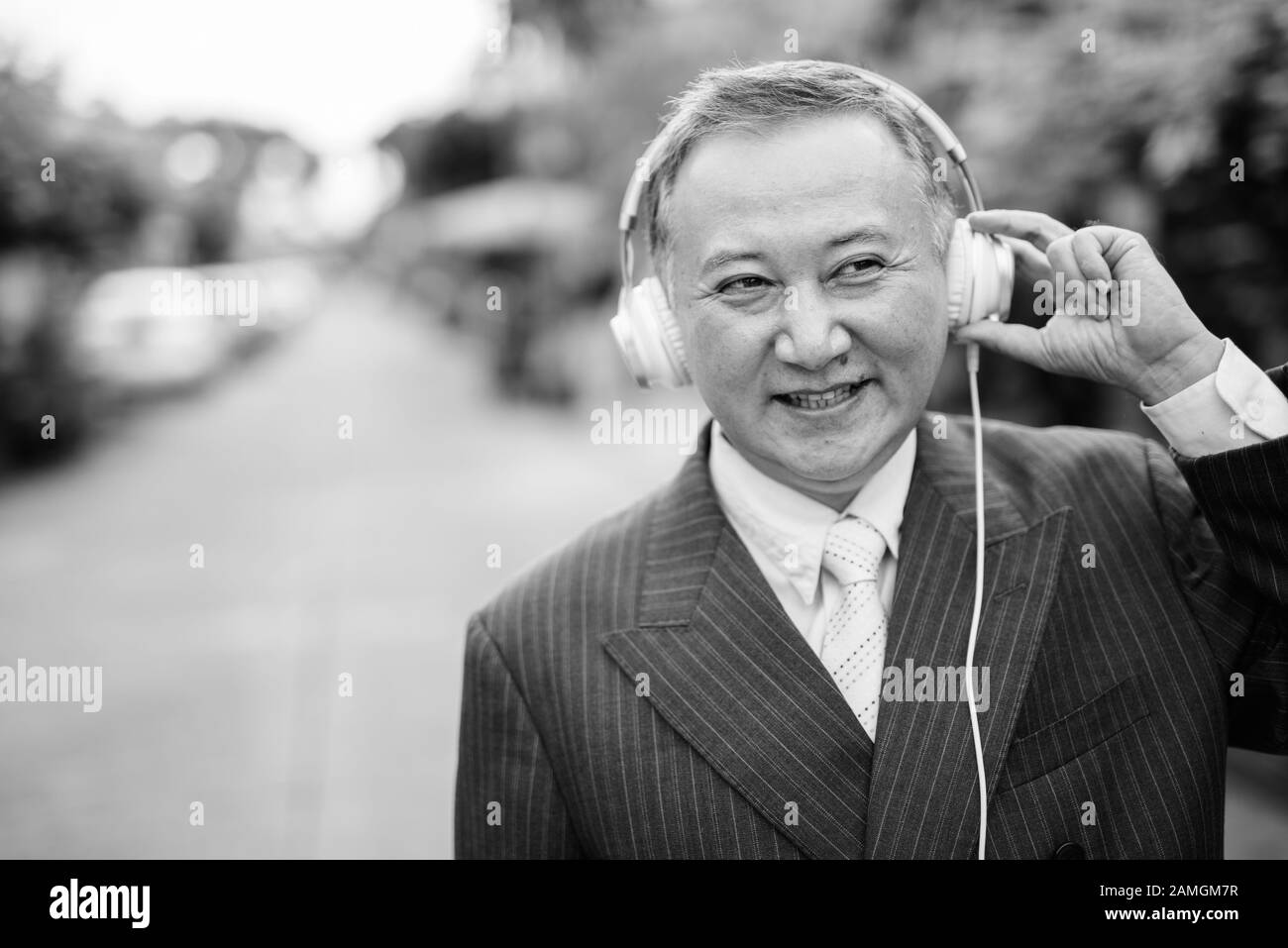 Porträt eines reifen asiatischen Geschäftsmannes, der Anzug trägt, während er im Freien Musik auf den Straßen hört Stockfoto