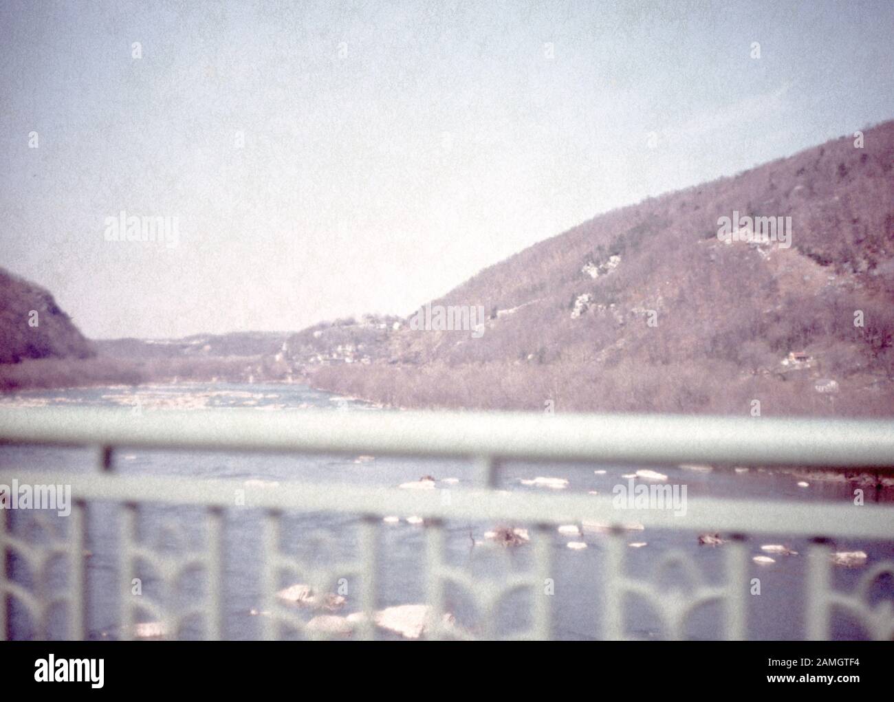 Nakuläres Foto, aufgenommen auf einer analogen 35-mm-Filmtransparenz, vermutlich, um weißen Metallzaun in der Nähe des Körpers von Wasser während des Tages, 1965, abzubilden. Wichtige Themen/Objekte, die erkannt wurden, sind Himmel, Berg, Natur und graue Farbe. () Stockfoto