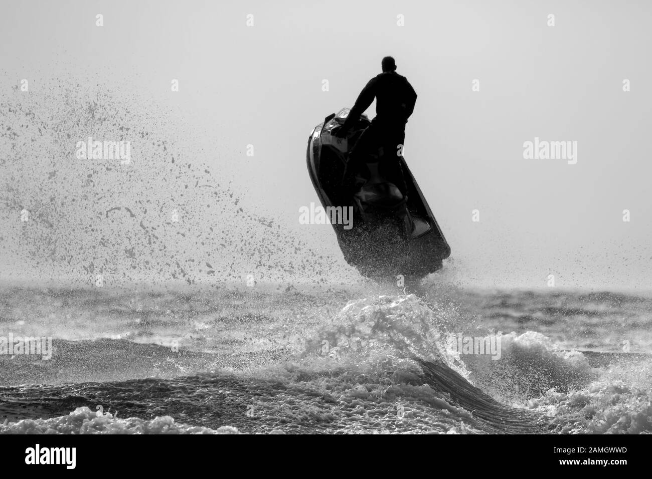 Dramatische, monochrome Action-Aufnahme von isolierten Mann auf Jet-Ski-Bike im Meer, in Silhouette, fliegen hoch in der Luft, Meeresspray, Wellen unten. Stockfoto